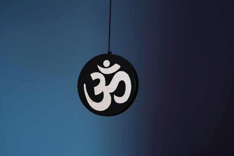 een wit ohm of aum teken op een zwarte, ronde hanger